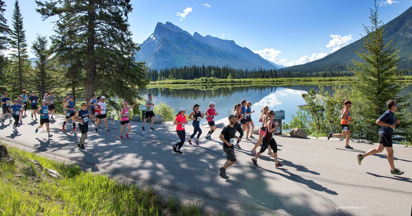 Marathon participants run beside lake under clear blue sky.