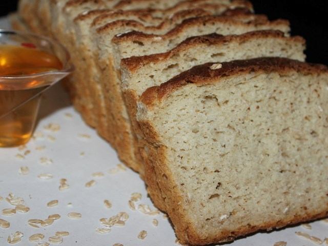 Gluten-free bread slices with honey and oats on a white surface.