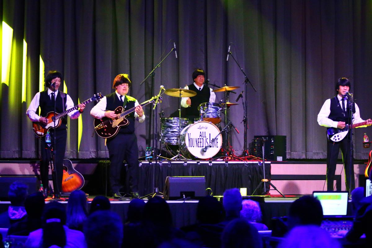 Live band performing on stage with colorful lights and audience in view.
