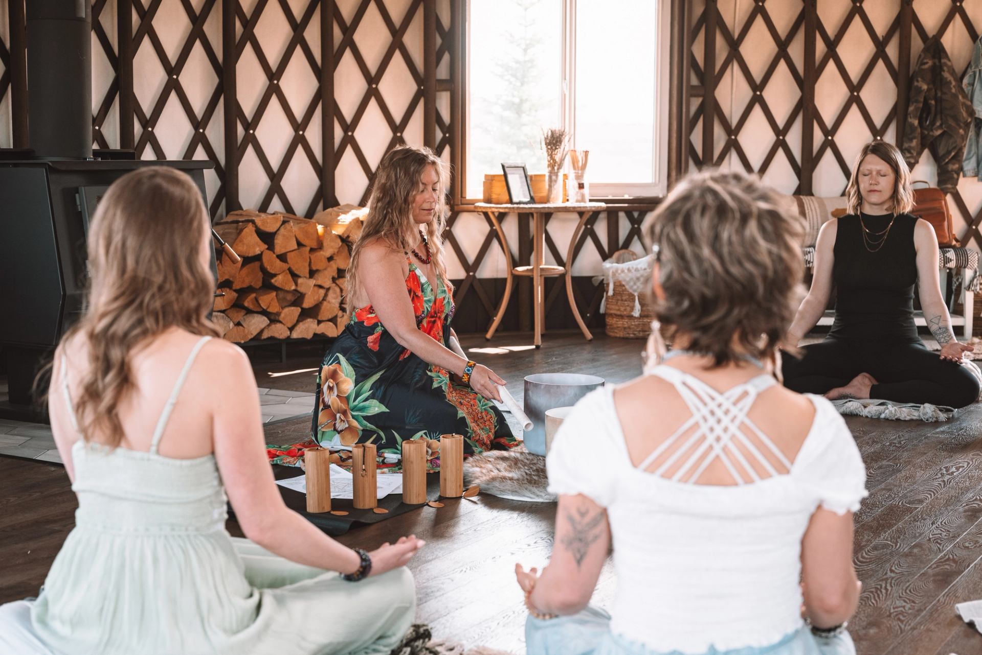 Group seated in meditation around singing bowls inside a lattice-walled room.