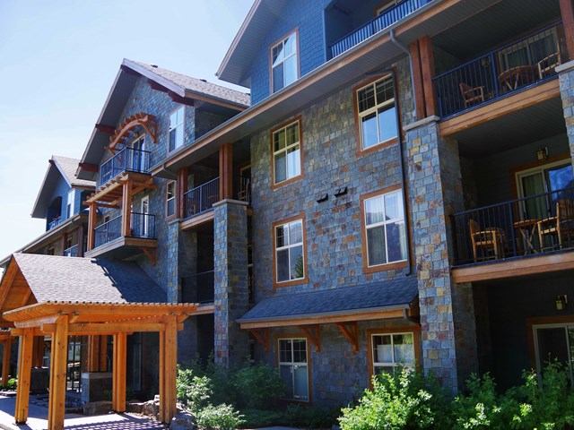 Rustic lodge exterior with stone and wood facade, balconies, and lush greenery.