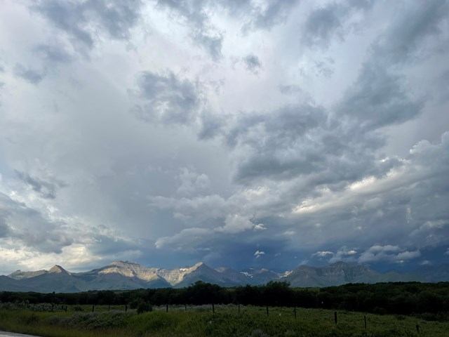 Grassy meadow and fence line with distant mountains under dark, layered clouds.