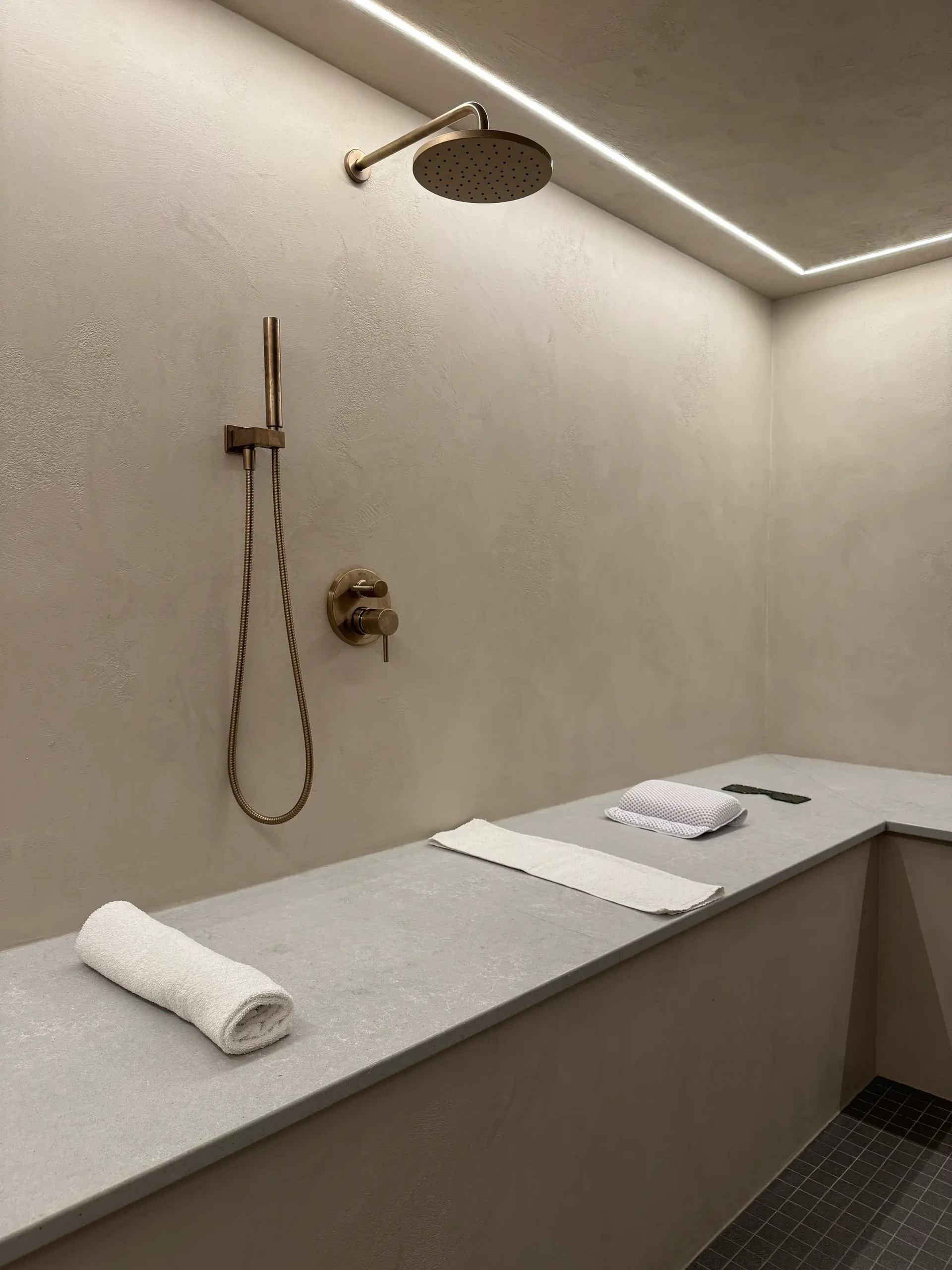 Minimal spa shower room with soft lighting, towels, and a sleek overhead shower.