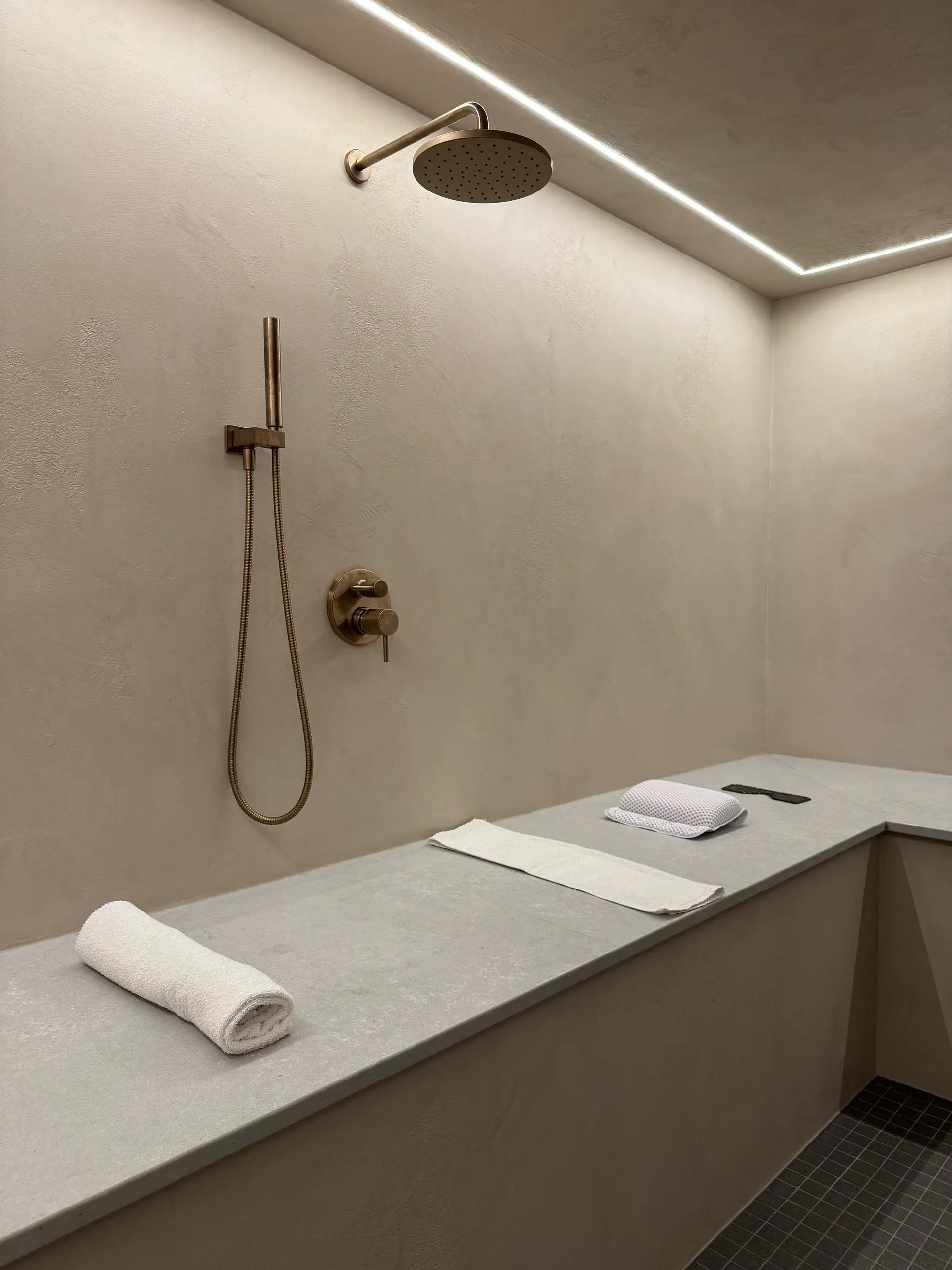Minimal spa shower room with soft lighting, towels, and a sleek overhead shower.