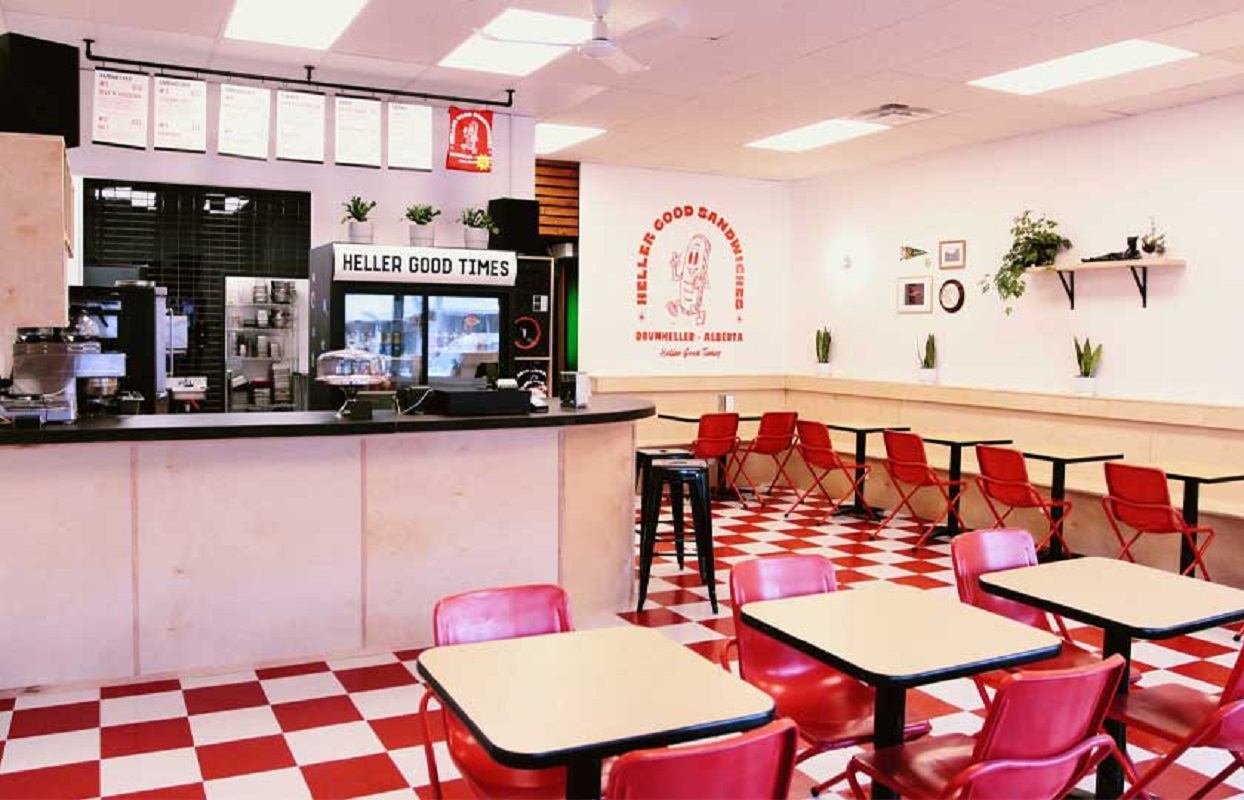 "Interior of a sandwich shop with red chairs, checkered floor, and a counter with the sign 'Heller Good Times.