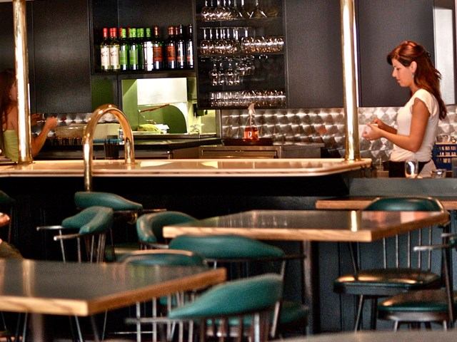Stylish bar interior with green chairs, wood tables, and a stocked counter.