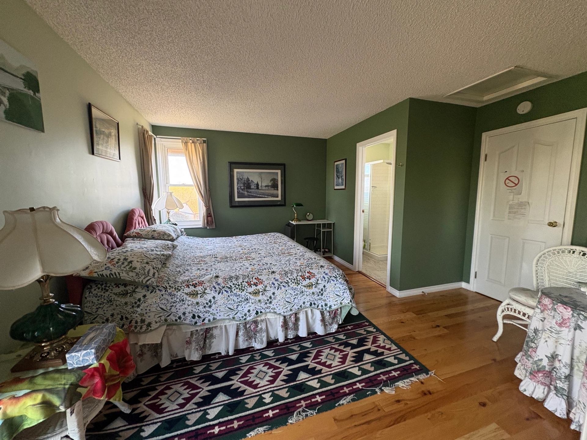 Bedroom with floral bedspread, green walls, hardwood floor and doorway to small bathroom.