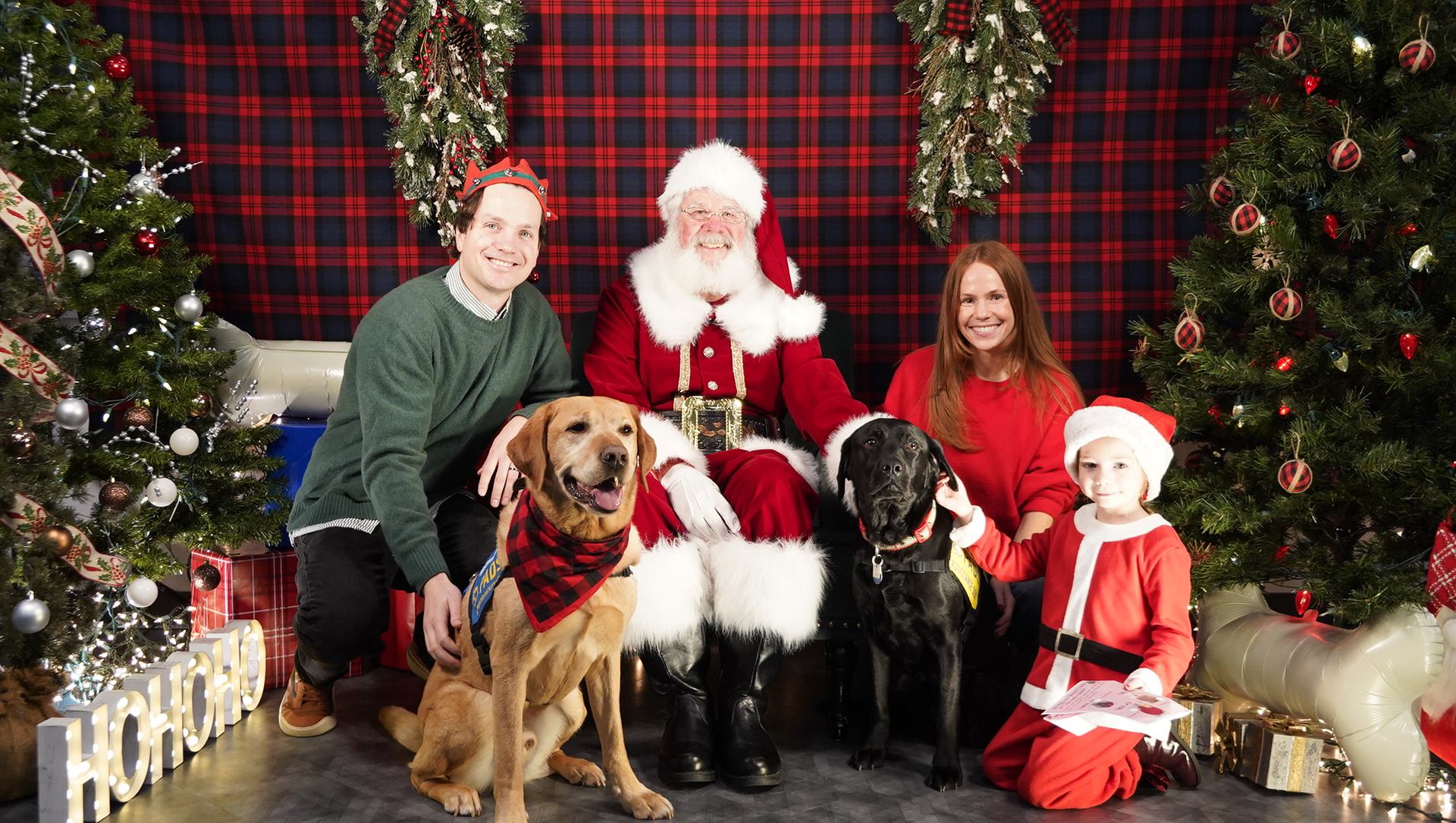Group poses with Santa, two dogs and decorated Christmas trees.