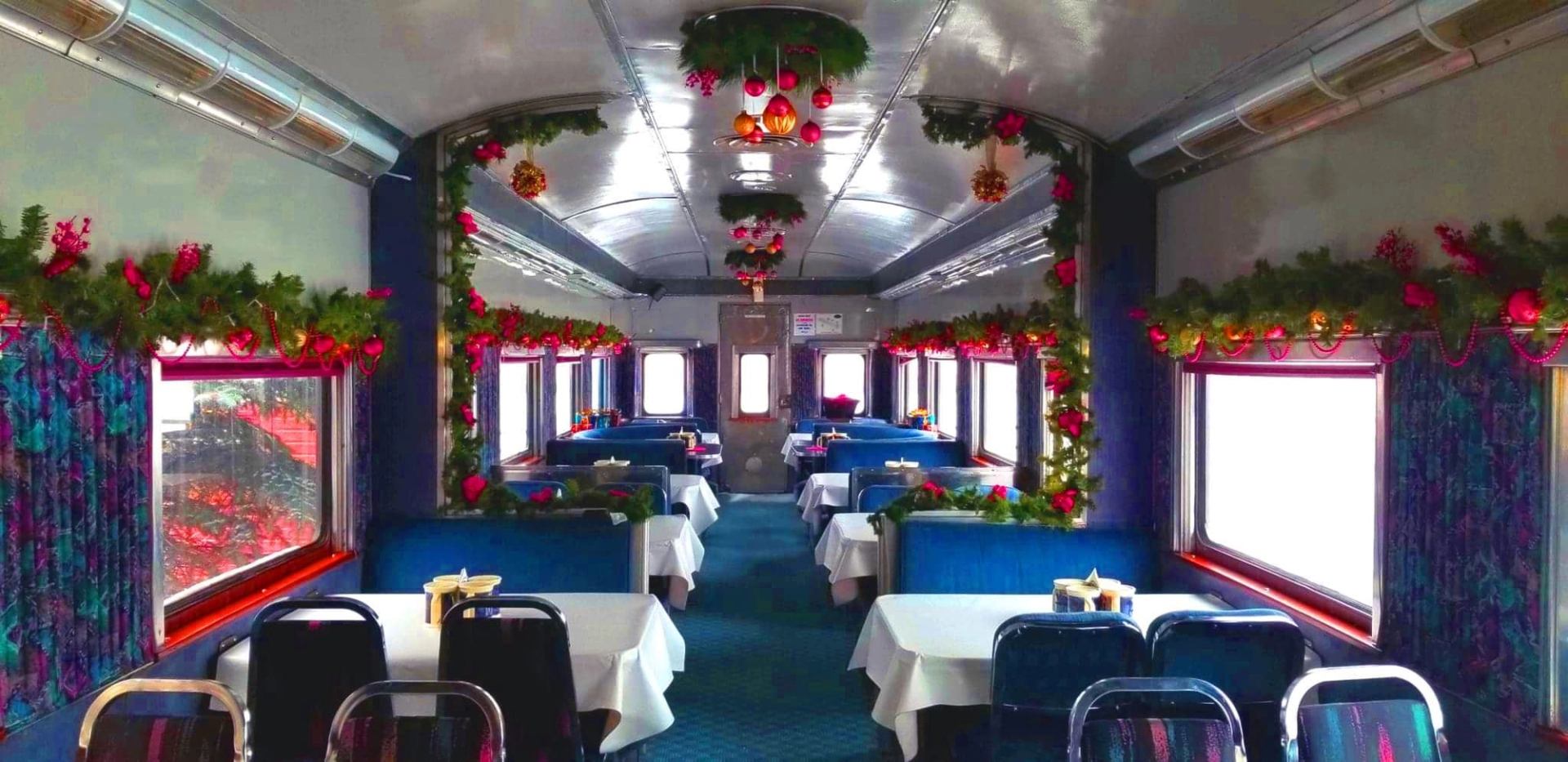 Dining car interior decorated with evergreen garlands, red ornaments and lights.