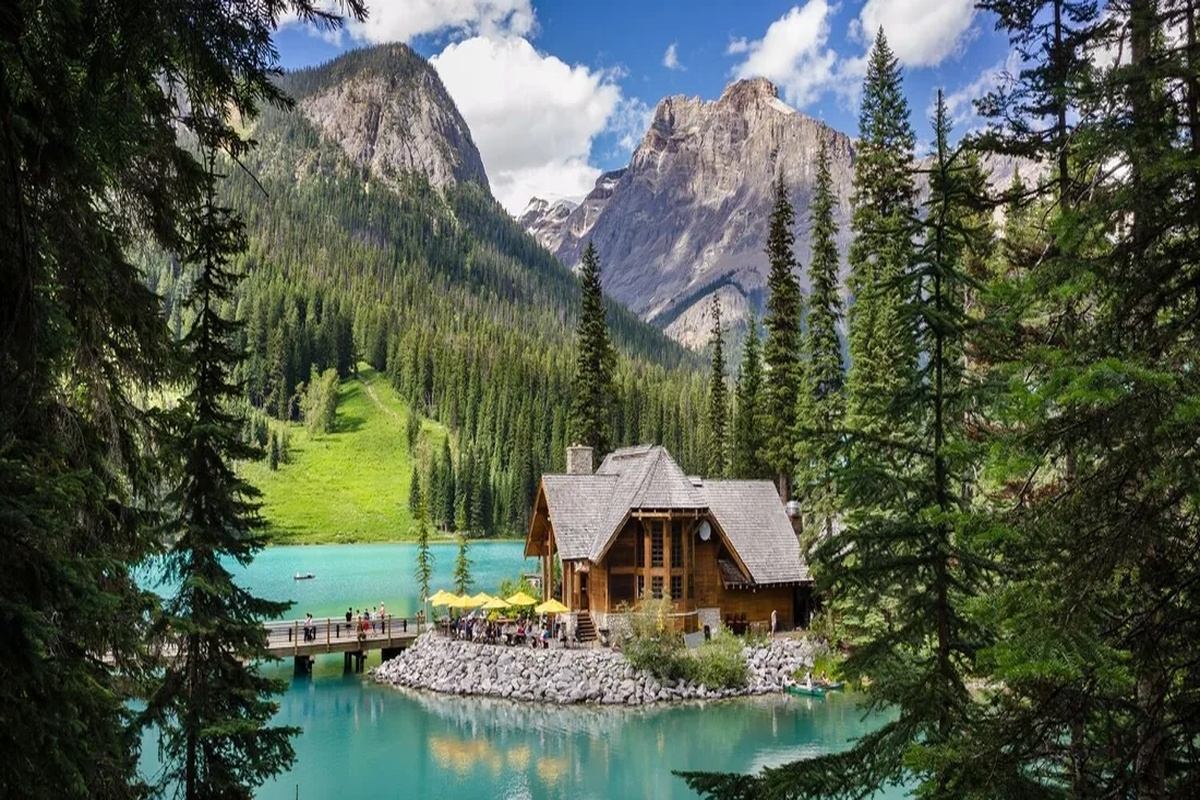 Wooden lodge beside a turquoise lake, surrounded by evergreens and rocky mountains.