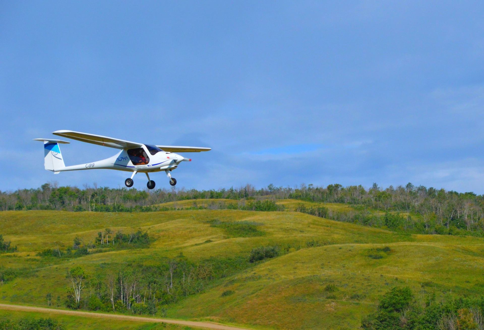 Ultralight aircraft flying over rolling green hills under a bright blue sky.