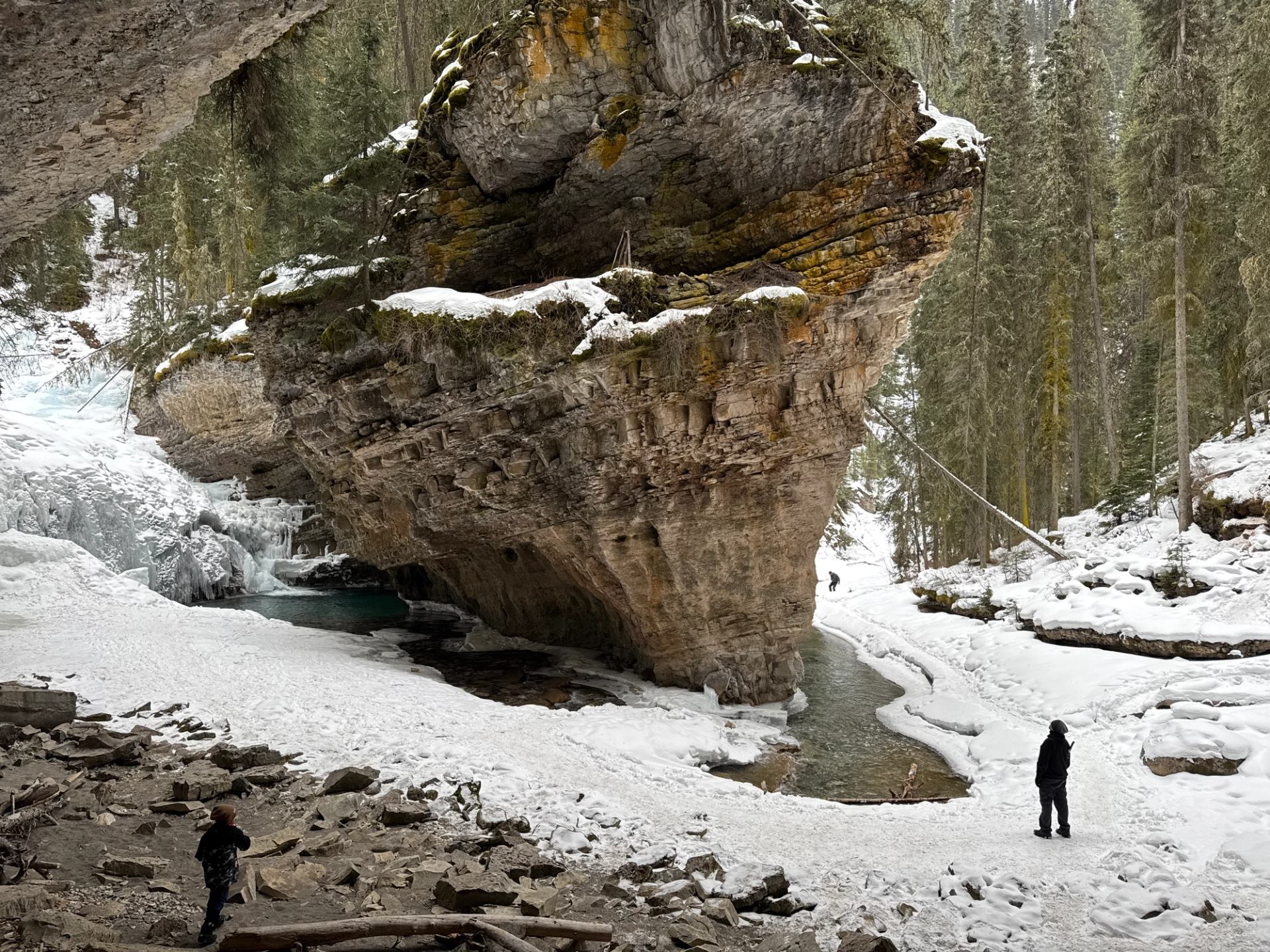 Two people exploring a snowy canyon with large rock formations and frozen water.