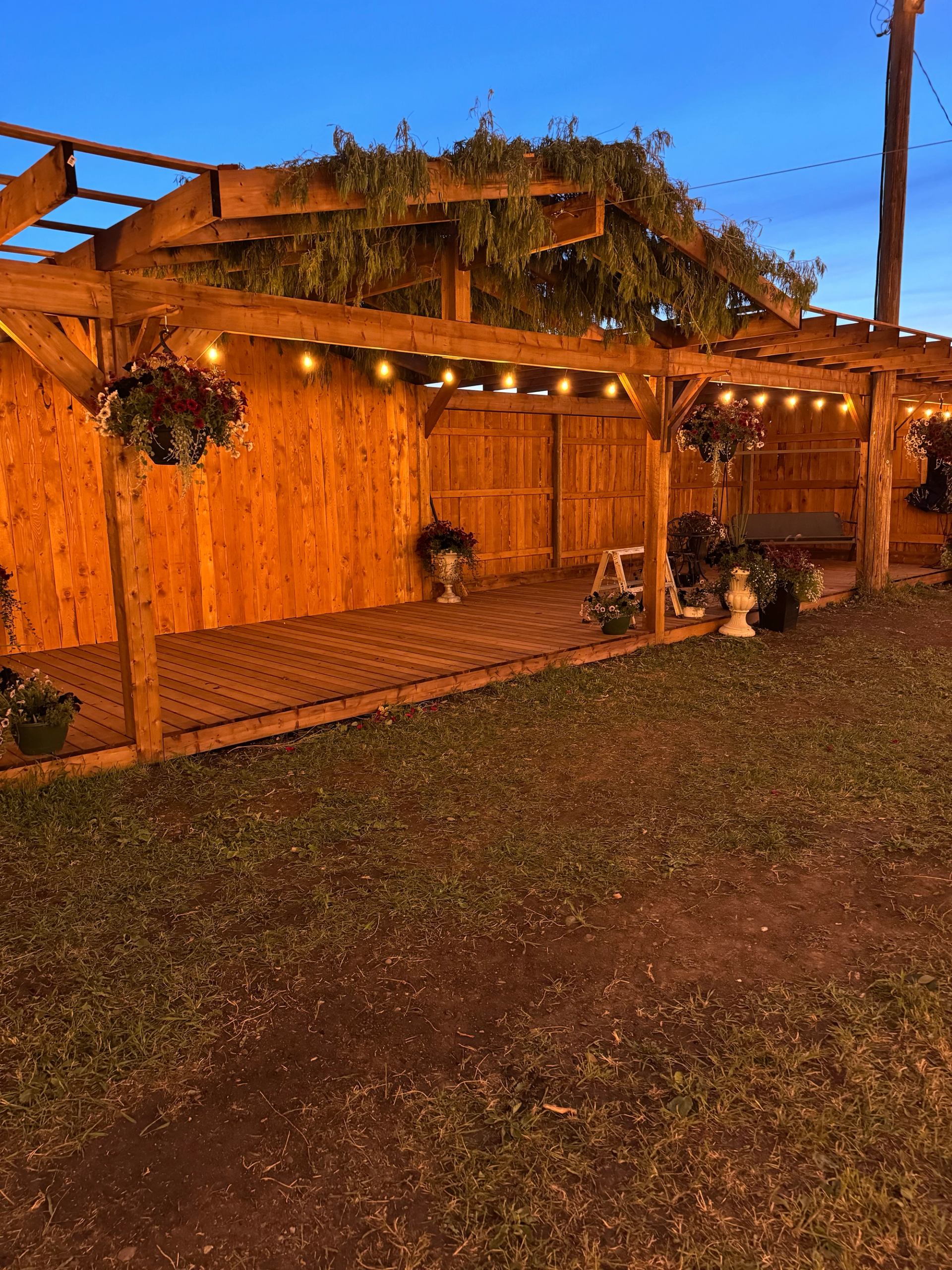 A wooden outdoor structure lit with string lights at dusk.