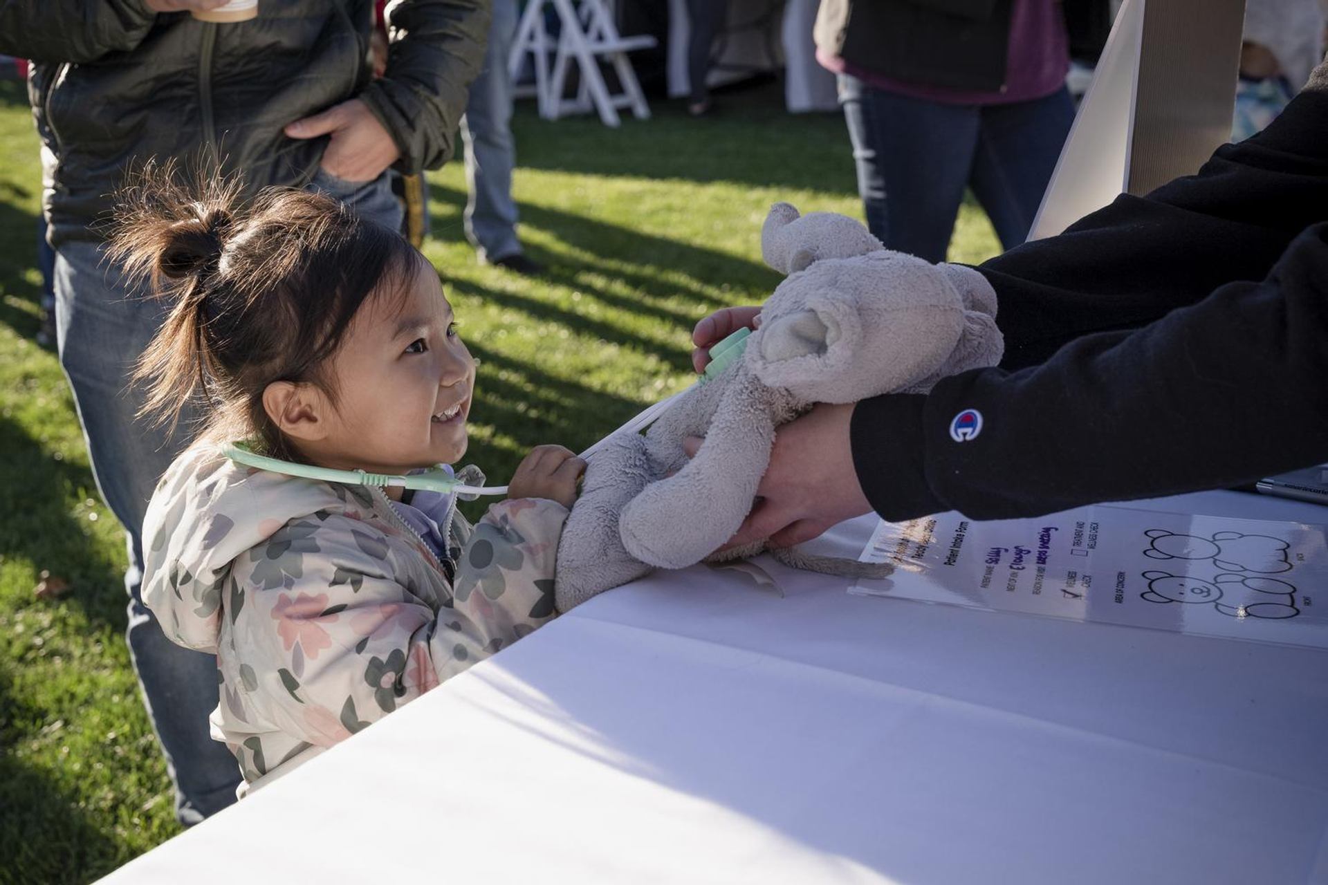 Child uses a toy stethoscope to examine a stuffed koala outdoors.