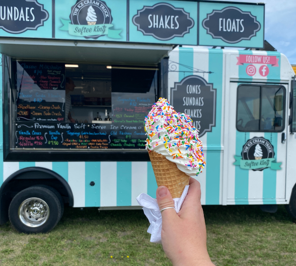Hand holding a sprinkle-covered ice cream cone in front of a dessert truck