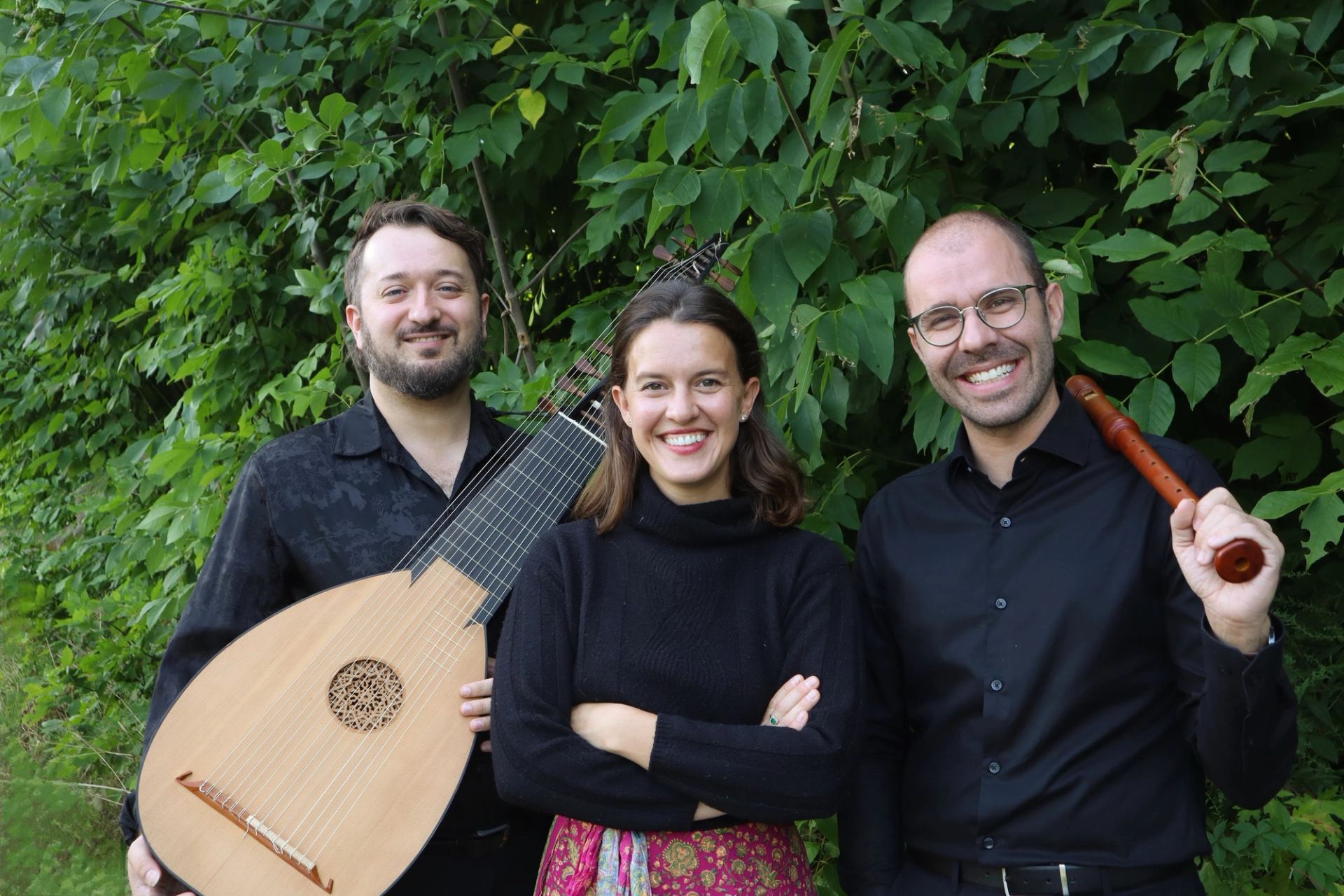 Three musicians stand before leafy bushes, holding a lute and wooden recorder.