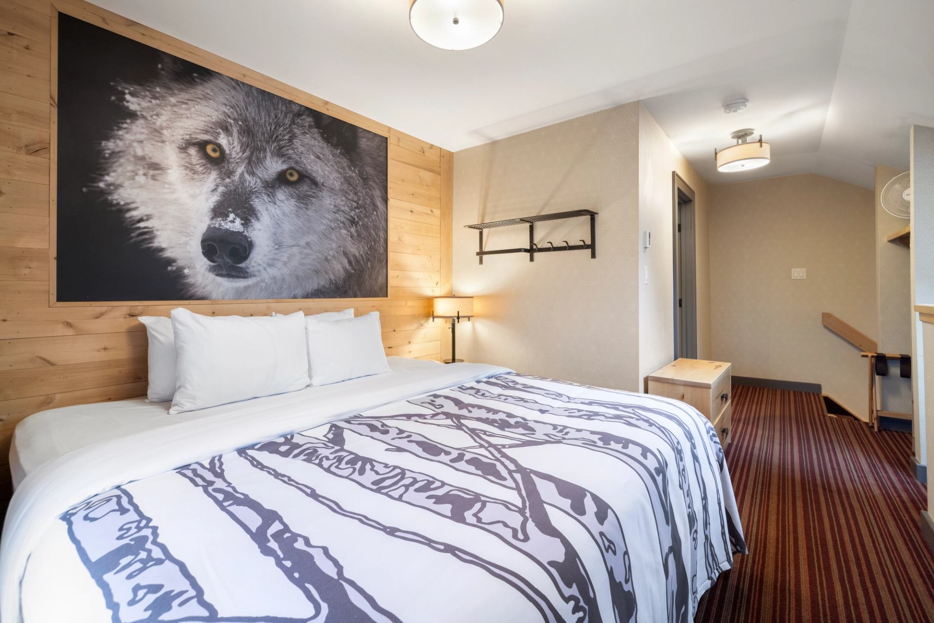 Kind size bed with a print of branches on the bedding, red carpet and a wolf photo on the wall.