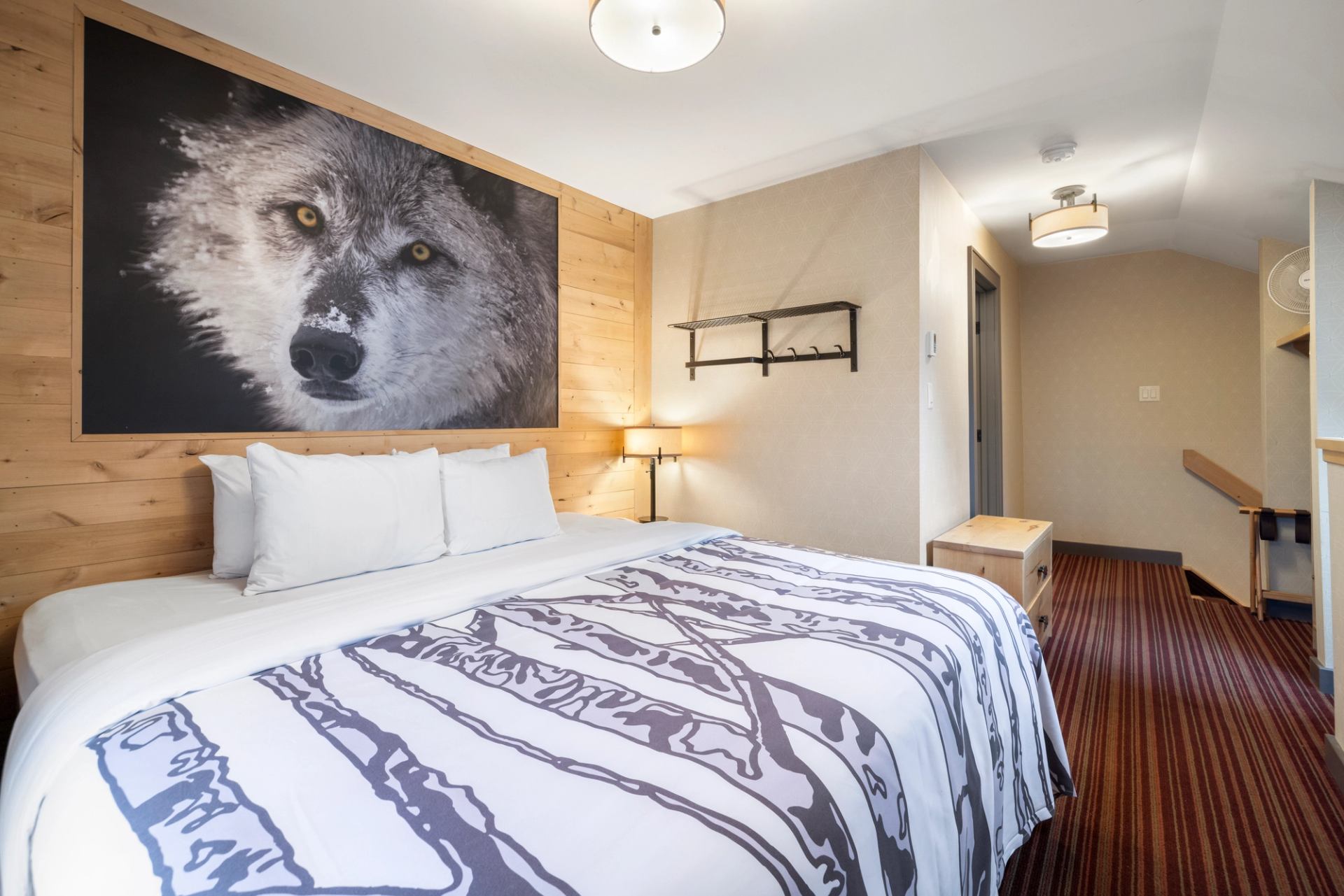 Kind size bed with a print of branches on the bedding, red carpet and a wolf photo on the wall.