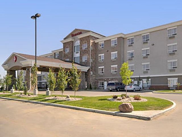 Exterior view of Ramada Camrose Hotel & Suites with parking area and landscaped entrance.