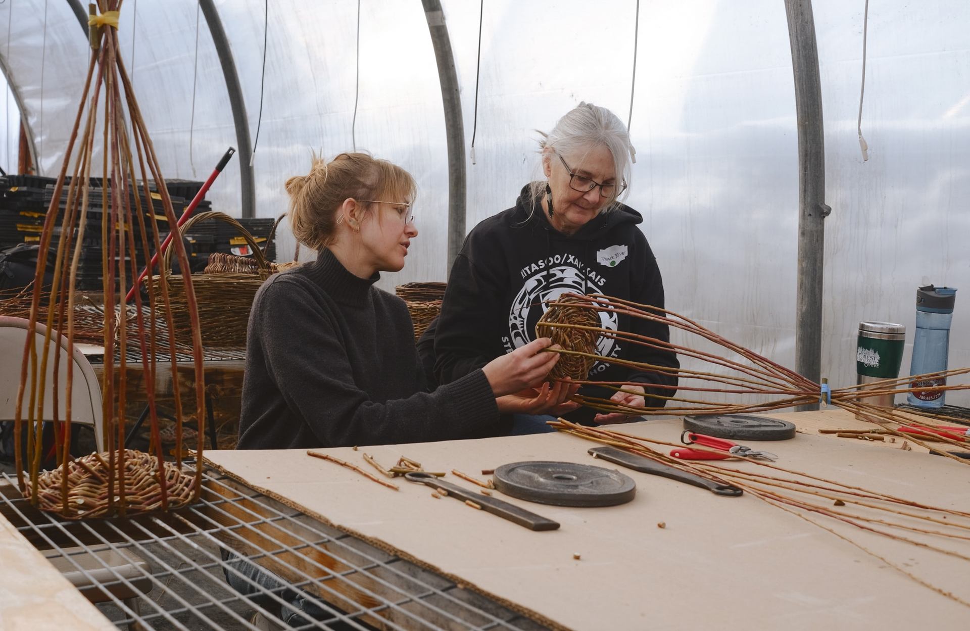 Two women discussing the bottom of a partially finished basket.