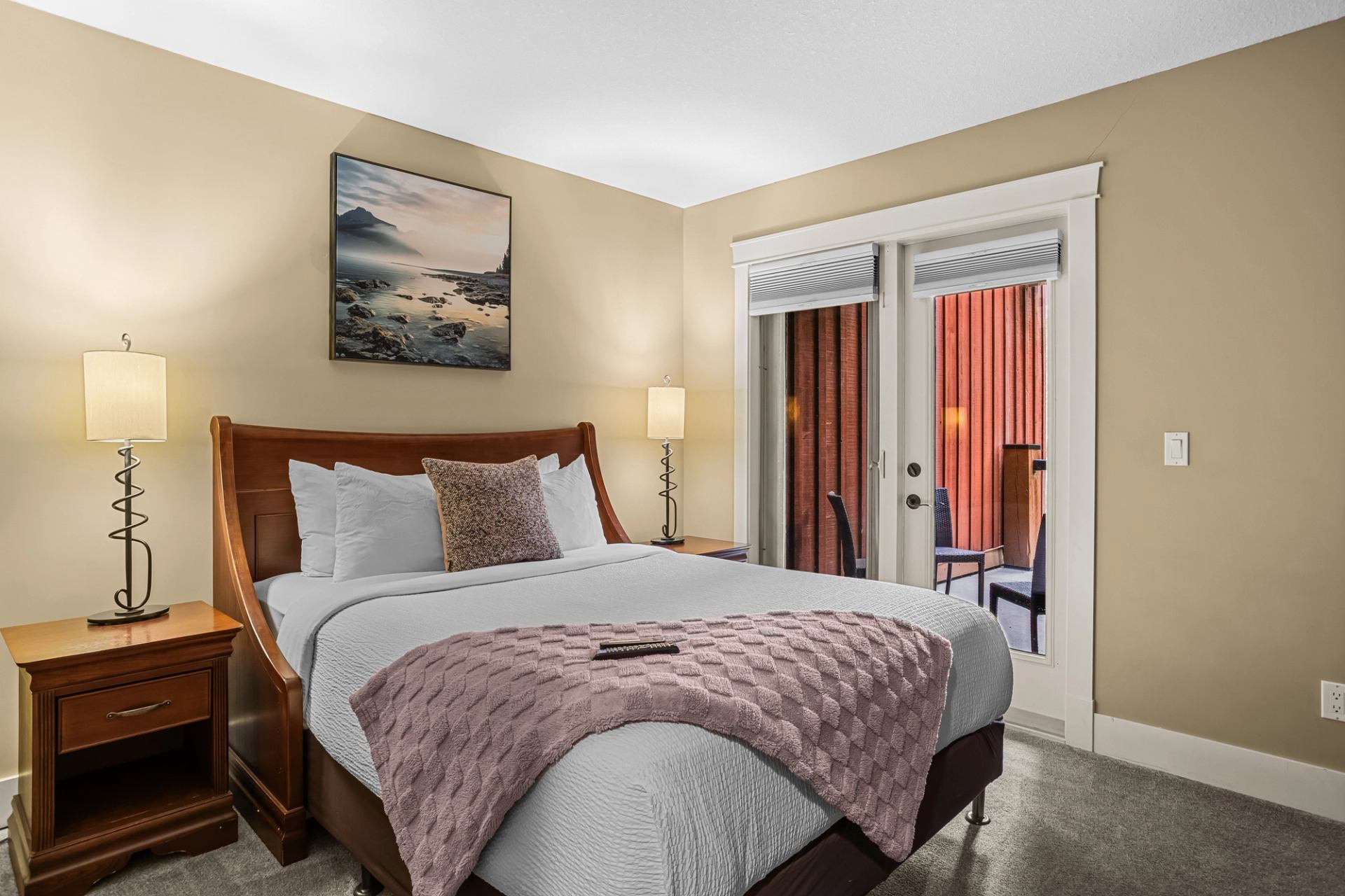 Bedroom with wooden bed, bedside lamps and glass doors opening to a balcony.