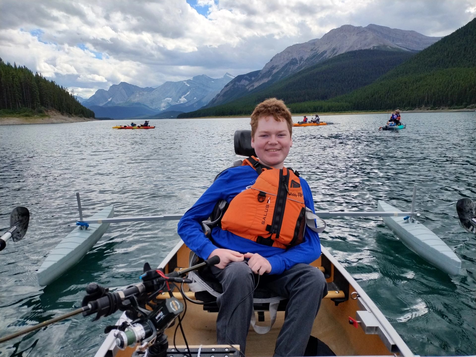 Person in an adaptive kayak on a mountain lake with calm water and scenic peaks.