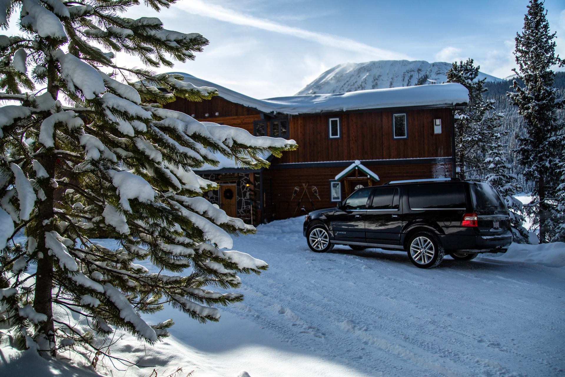 Black SUV parked outside a rustic wooden lodge surrounded by snow and mountain scenery