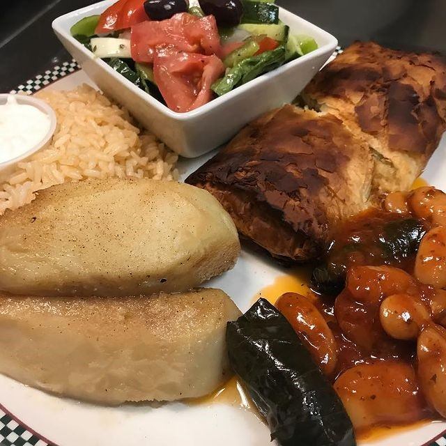Greek platter with baked pastry, rice, salad, potatoes, and stuffed grape leaves.