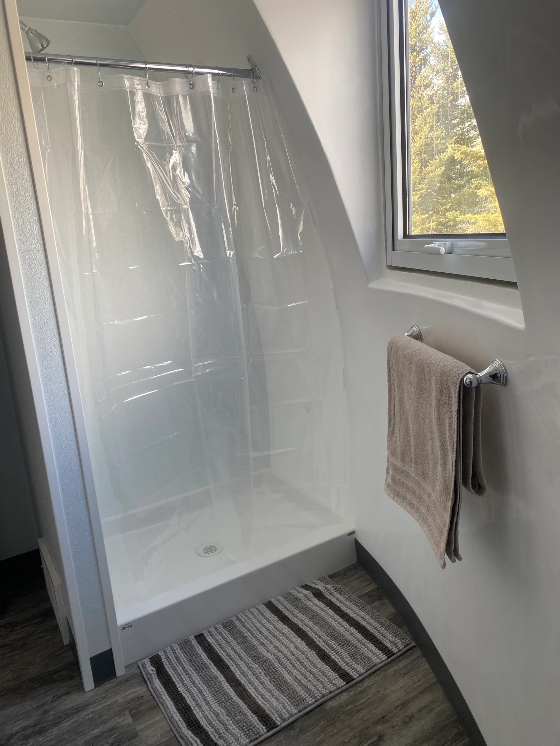 Dome bathroom with glass shower, window, and striped bath mats.