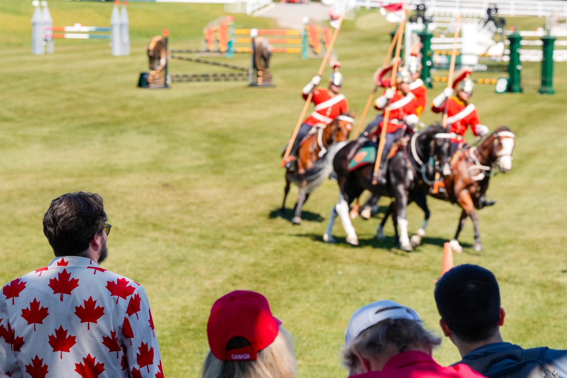 Mounted performers in red uniforms riding across a grassy arena