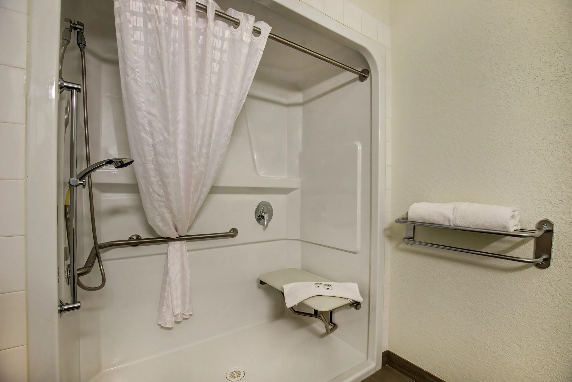 Walk-in shower with grab bars, handheld showerhead, and foldable seat for accessibility.