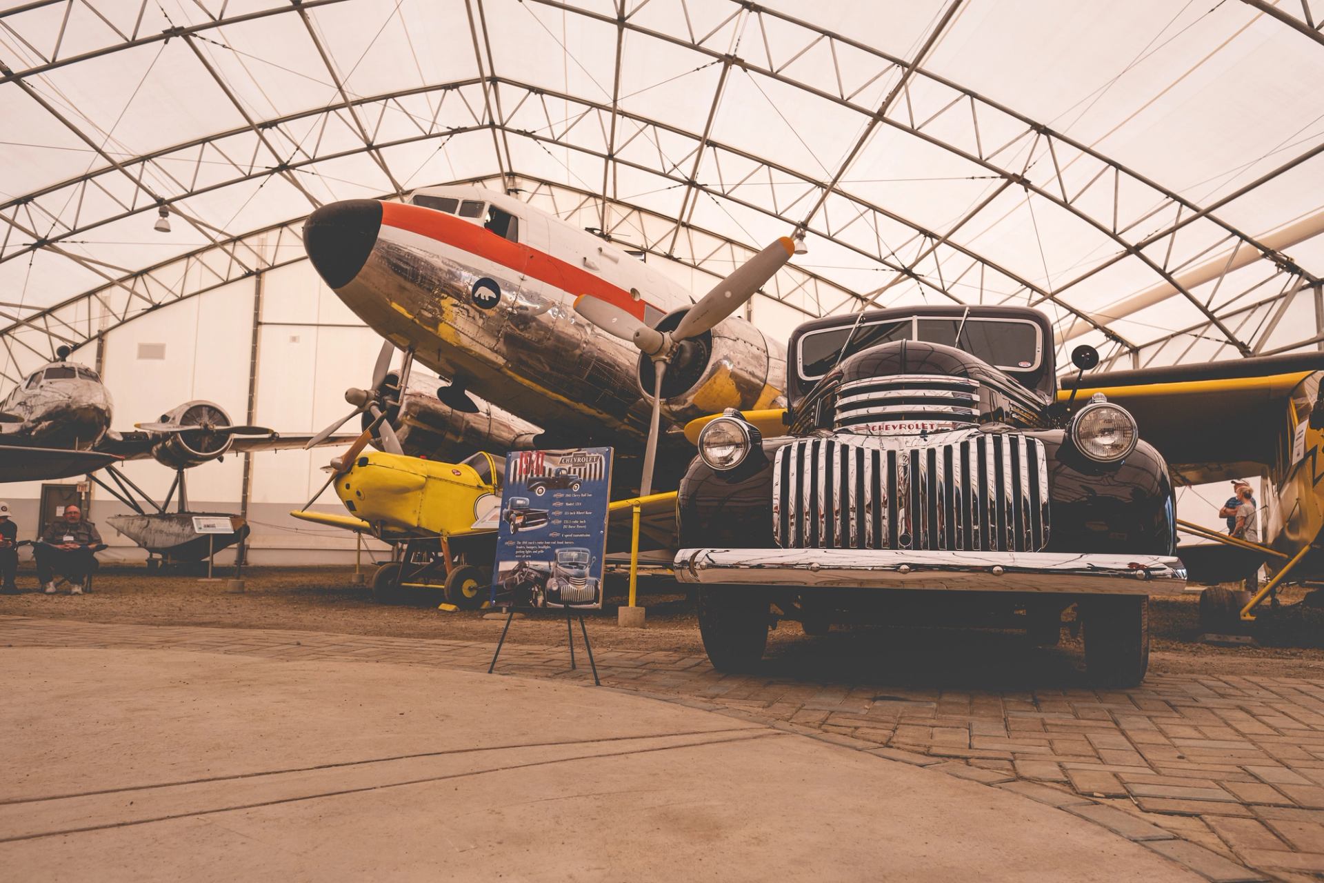 Vintage airplane and classic Chevrolet truck displayed inside a large hangar.
