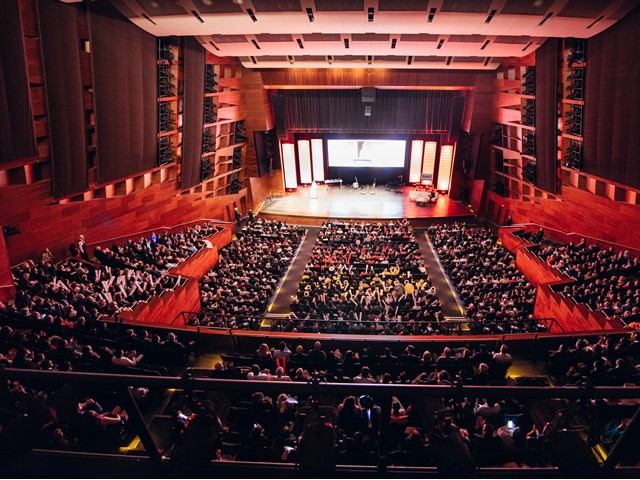 Theatre auditorium with stage lights, rows of seats, and audience in view.