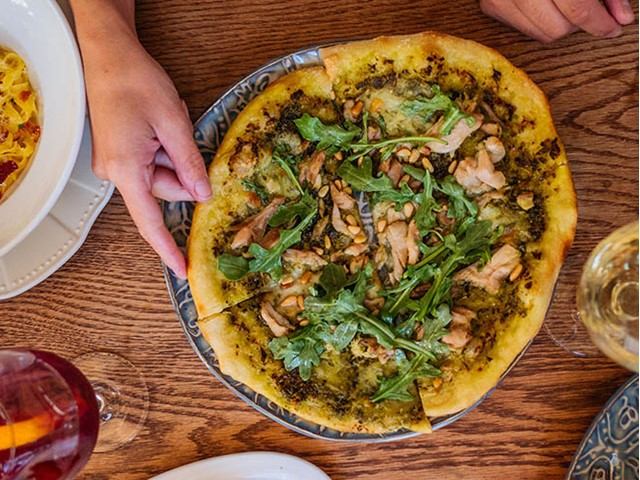 Chicken pizza with greens and pine nuts, served with white wine.