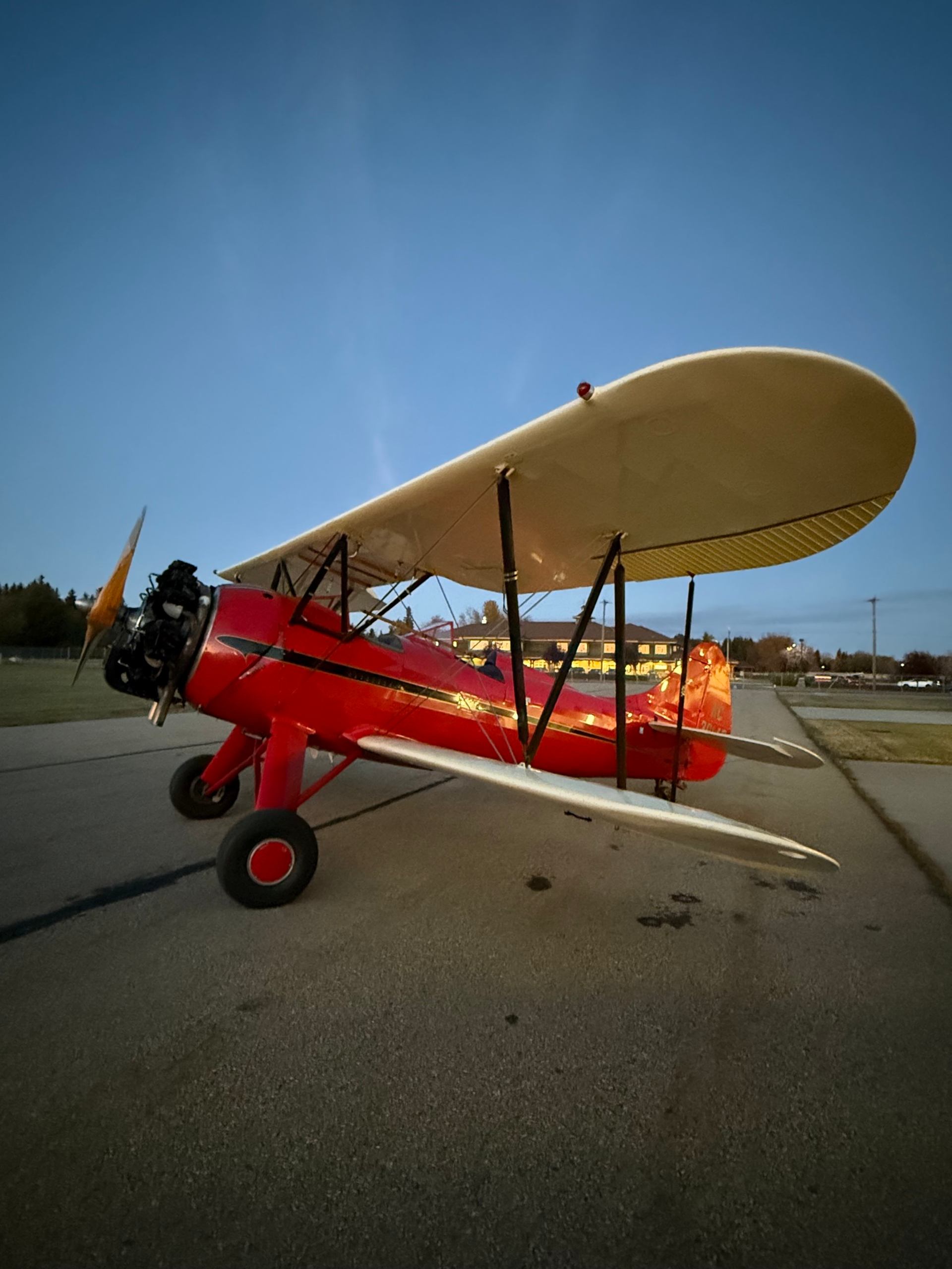 Red vintage biplane parked on airport tarmac under clear blue sky.