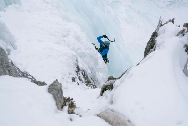 An ice climber surrounded by snow and ice, uses his ice pick at Tangle Falls in Jasper National Park