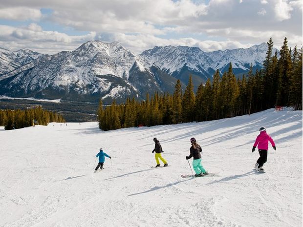 Four people skiing and snowboarding at Nakiska Ski Resort with views of the mountains in Kananaskis Country