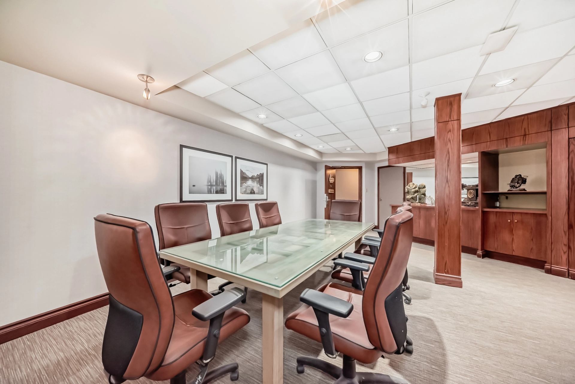 Meeting room featuring a glass table, leather chairs, and framed pictures on the wall