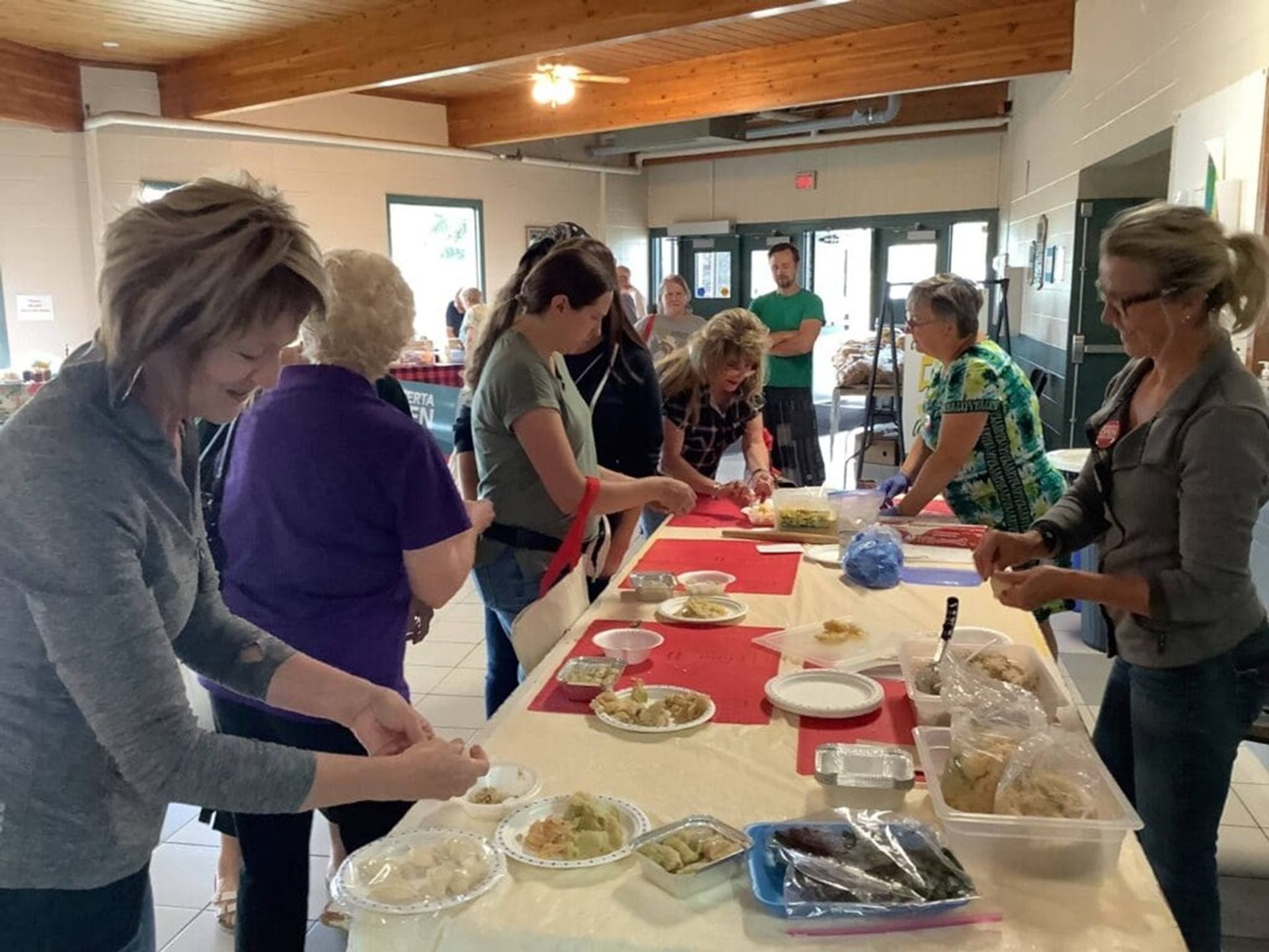 Community members gather around tables indoors, preparing food and arranging dishes together.