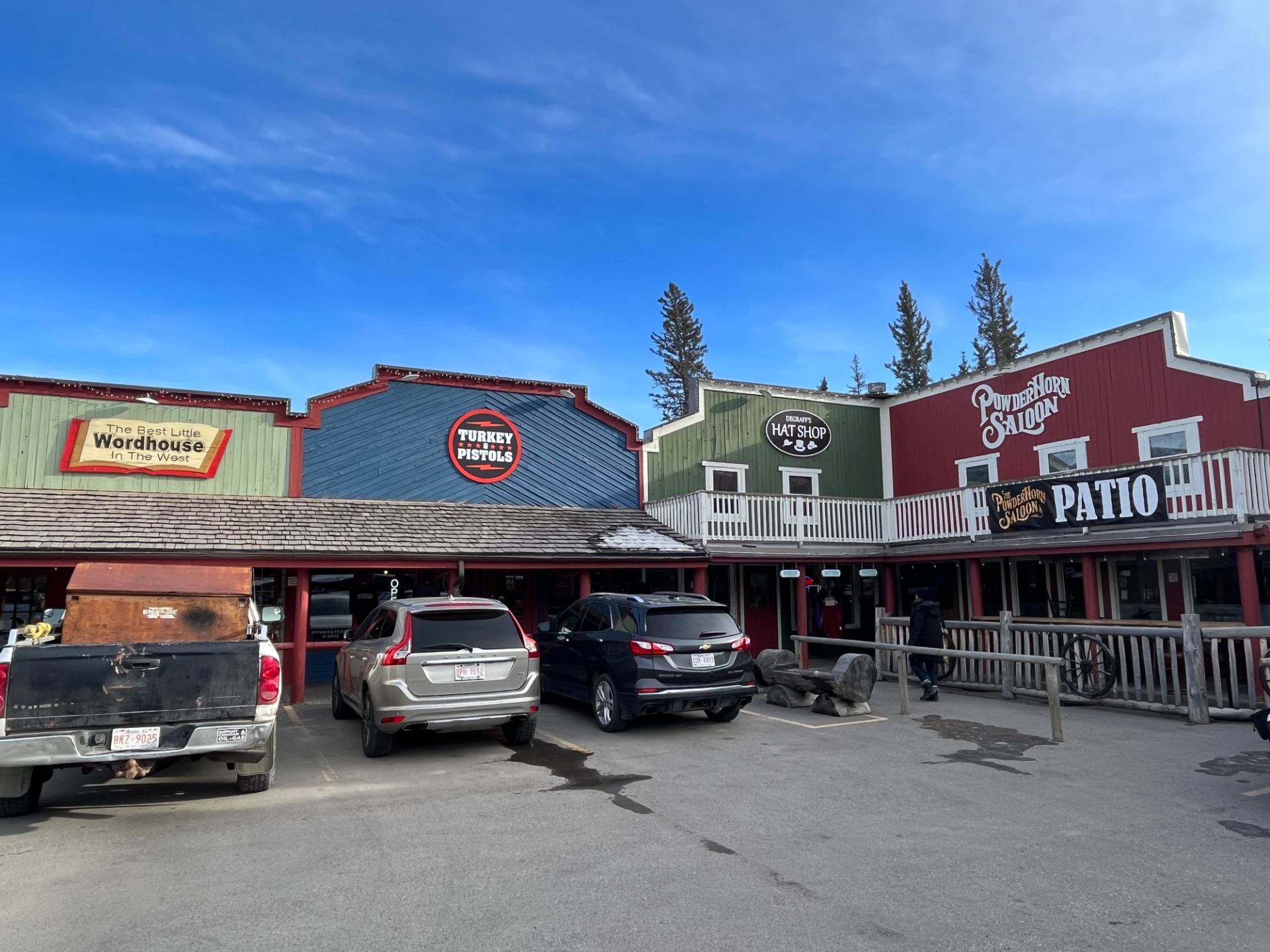 Colorful wooden storefronts in Bragg Creek with parked cars and blue skies.