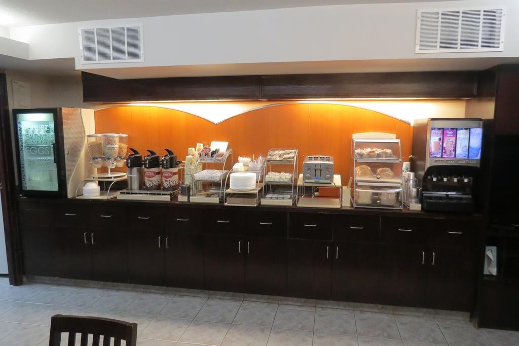 Hotel breakfast buffet counter with appliances, food trays, and beverage dispensers.