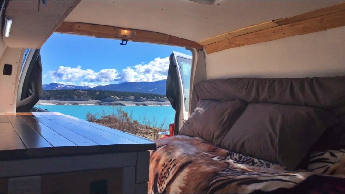 Cozy camper van with lake and mountain view through open doors.