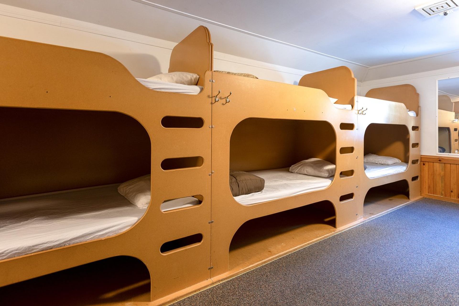 Shared bunk room with wooden beds, carpeted floor, and warm lighting.
