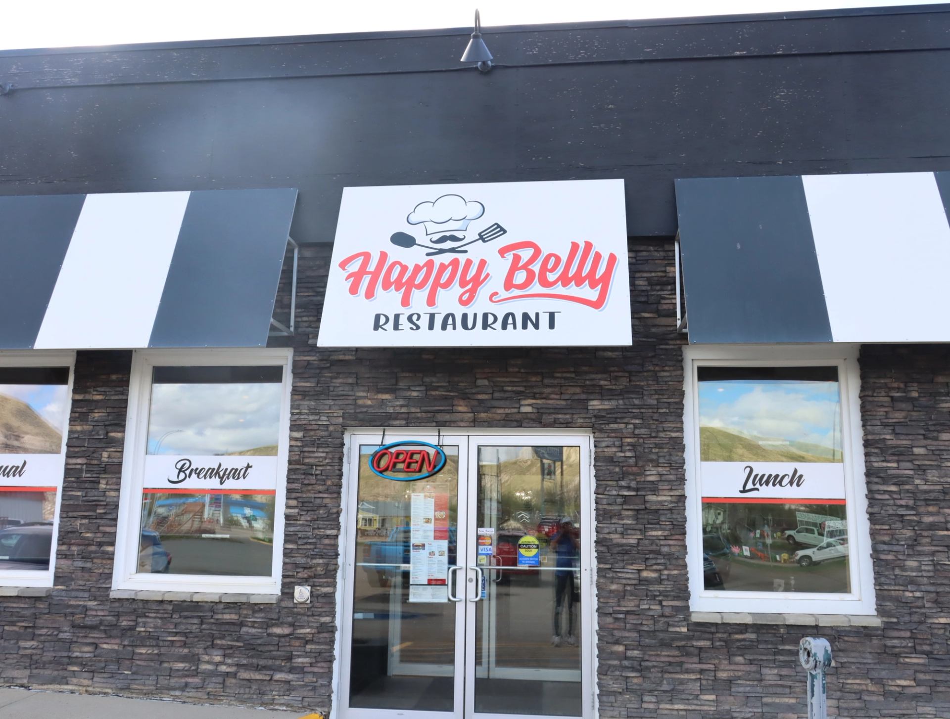 Happy Belly Restaurant storefront with striped awnings, glass door and breakfast, lunch signs.