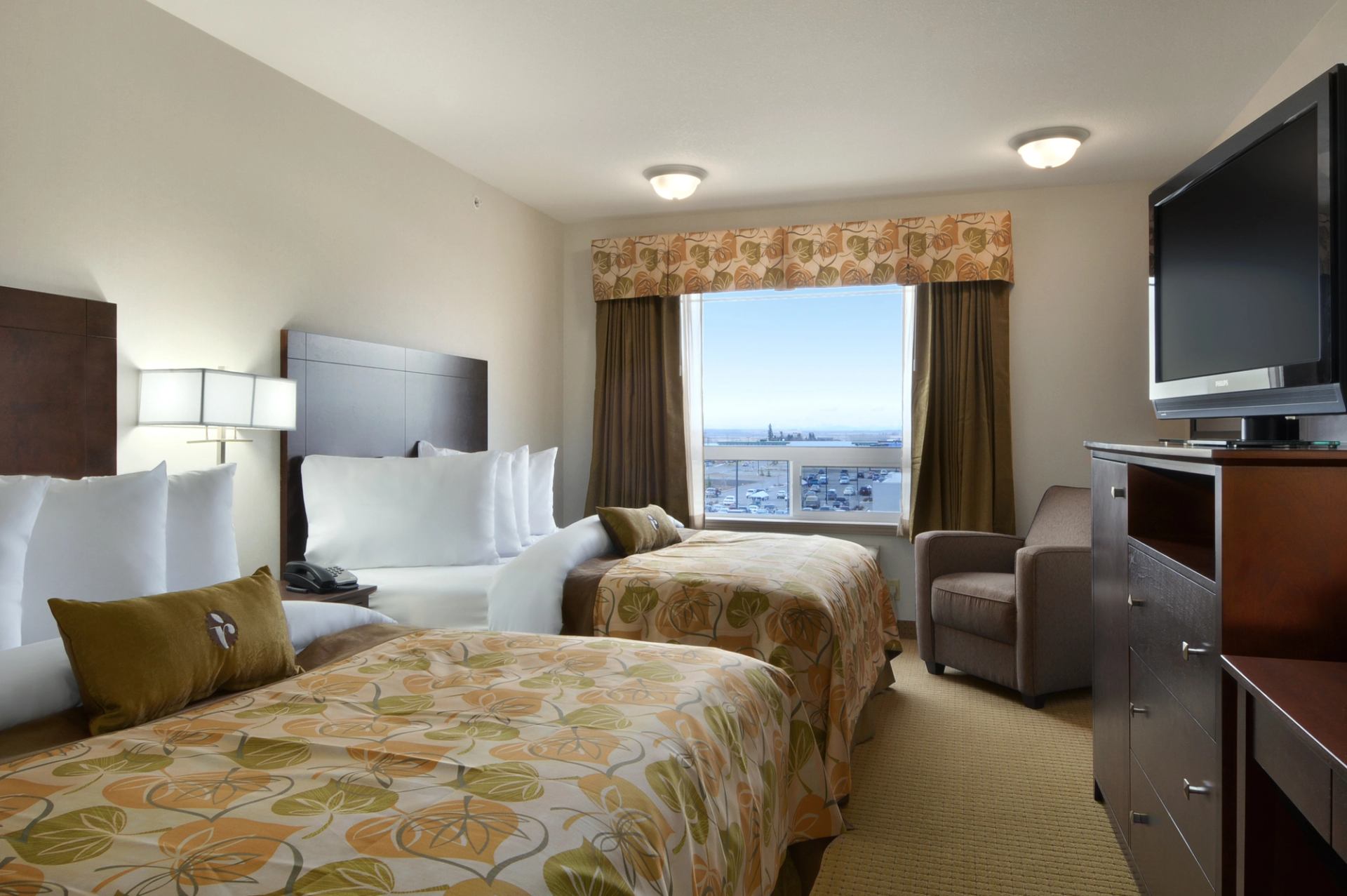 Hotel room with two beds, armchair, television and harbour view through window.