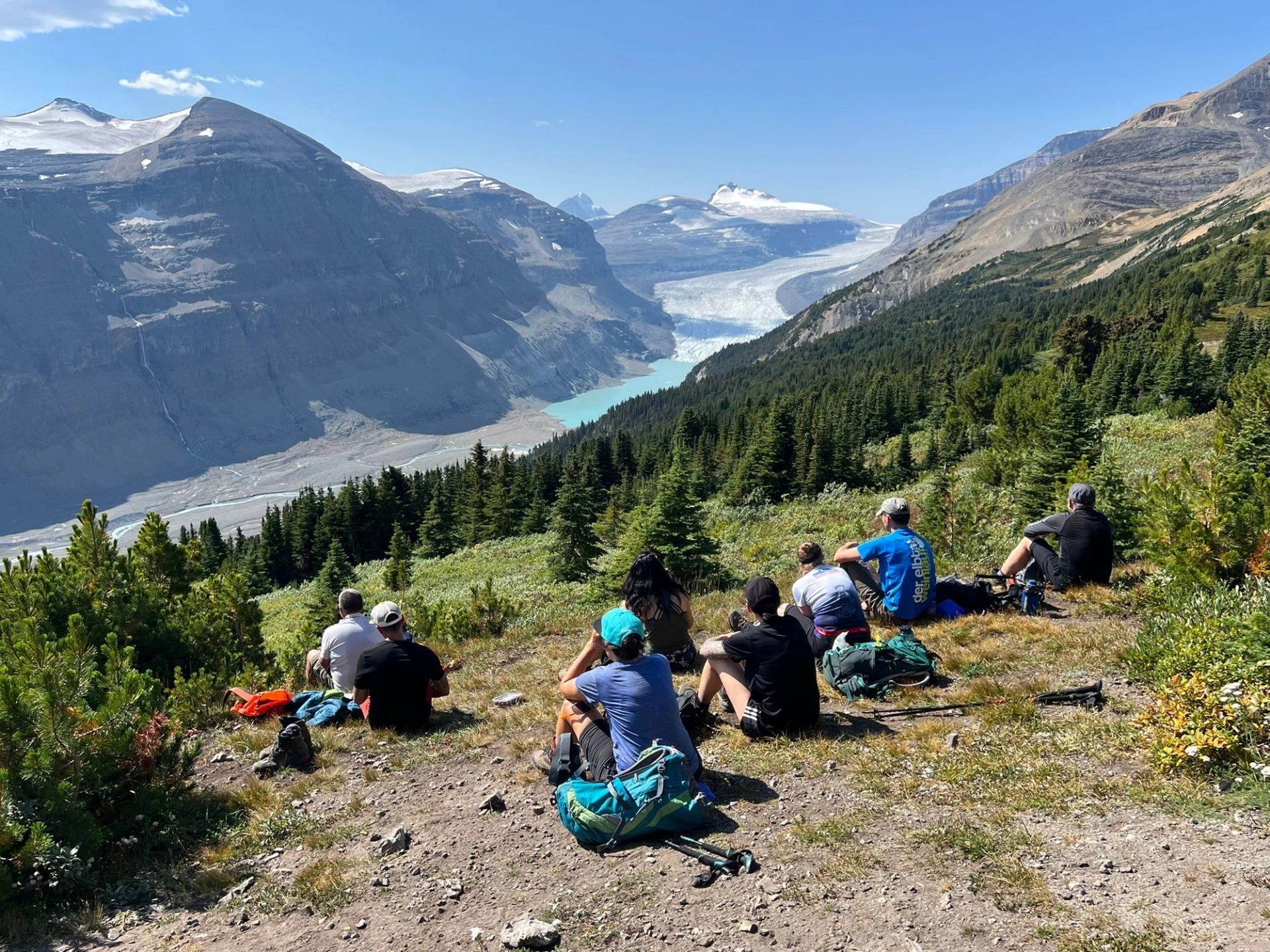 Group of hikers sitting in the grass high above a glacier filled valley.