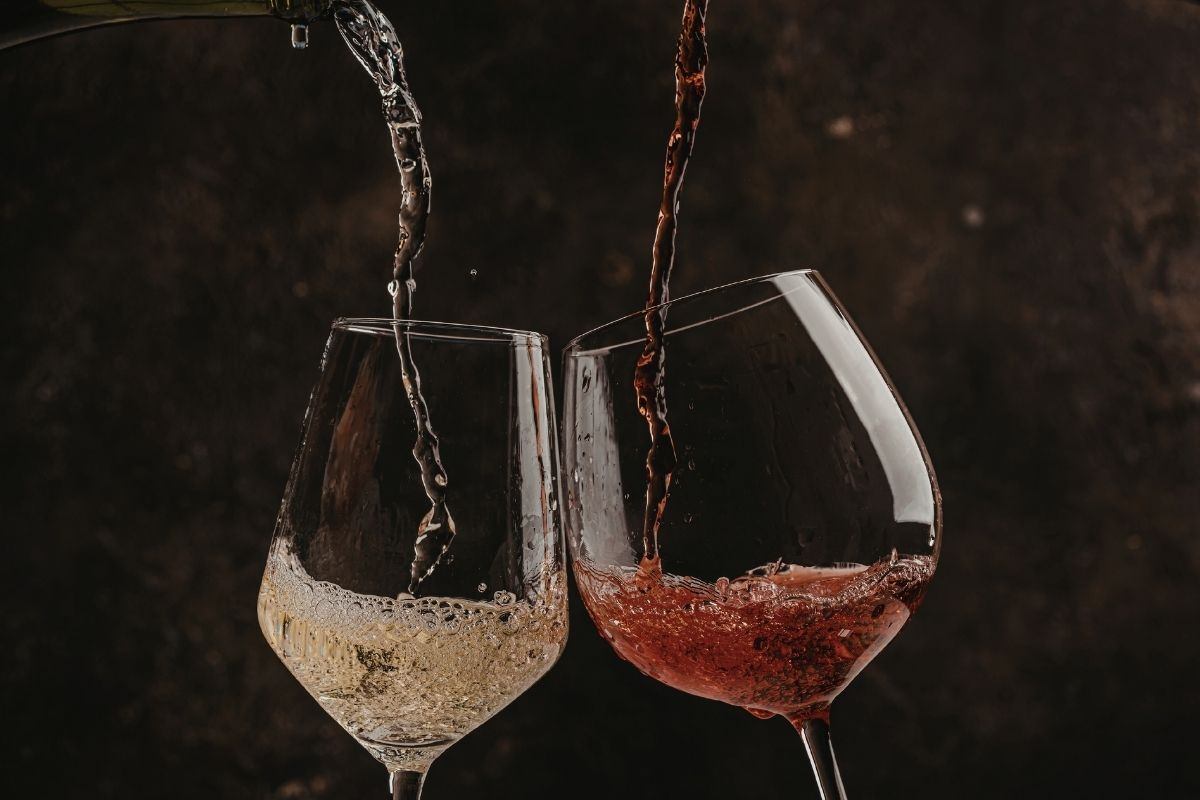 White and red wine being poured into two glasses.