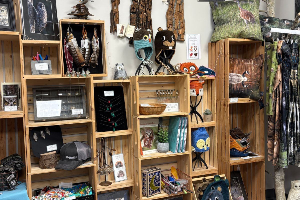 Medicine River Wildlife Centre gift shop displays handmade items, wildlife-themed apparel, books, and artwork on wooden shelves.
