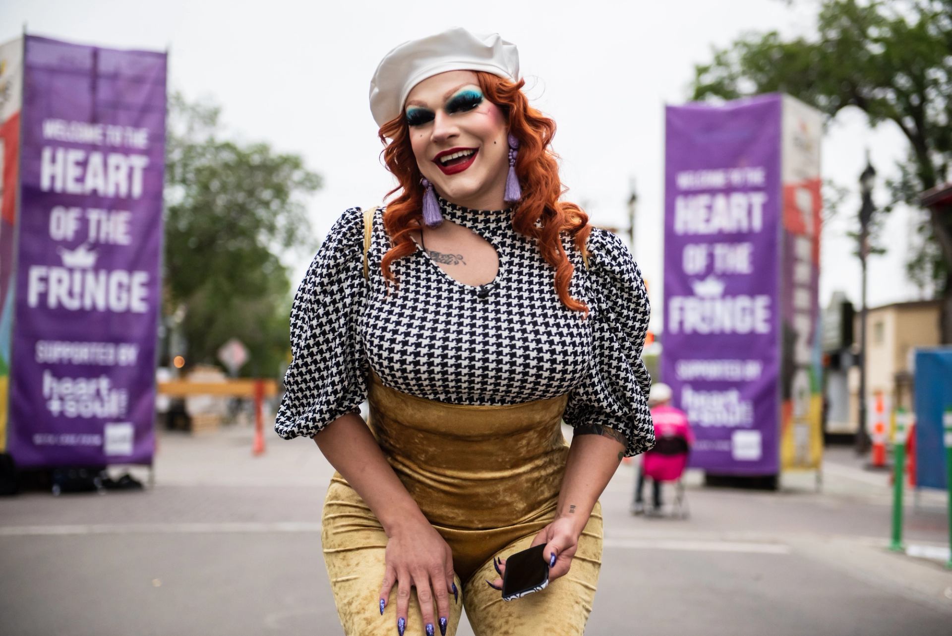 Performer in costume and hat, with purple “Heart of the Fringe” banners in Edmonton background.