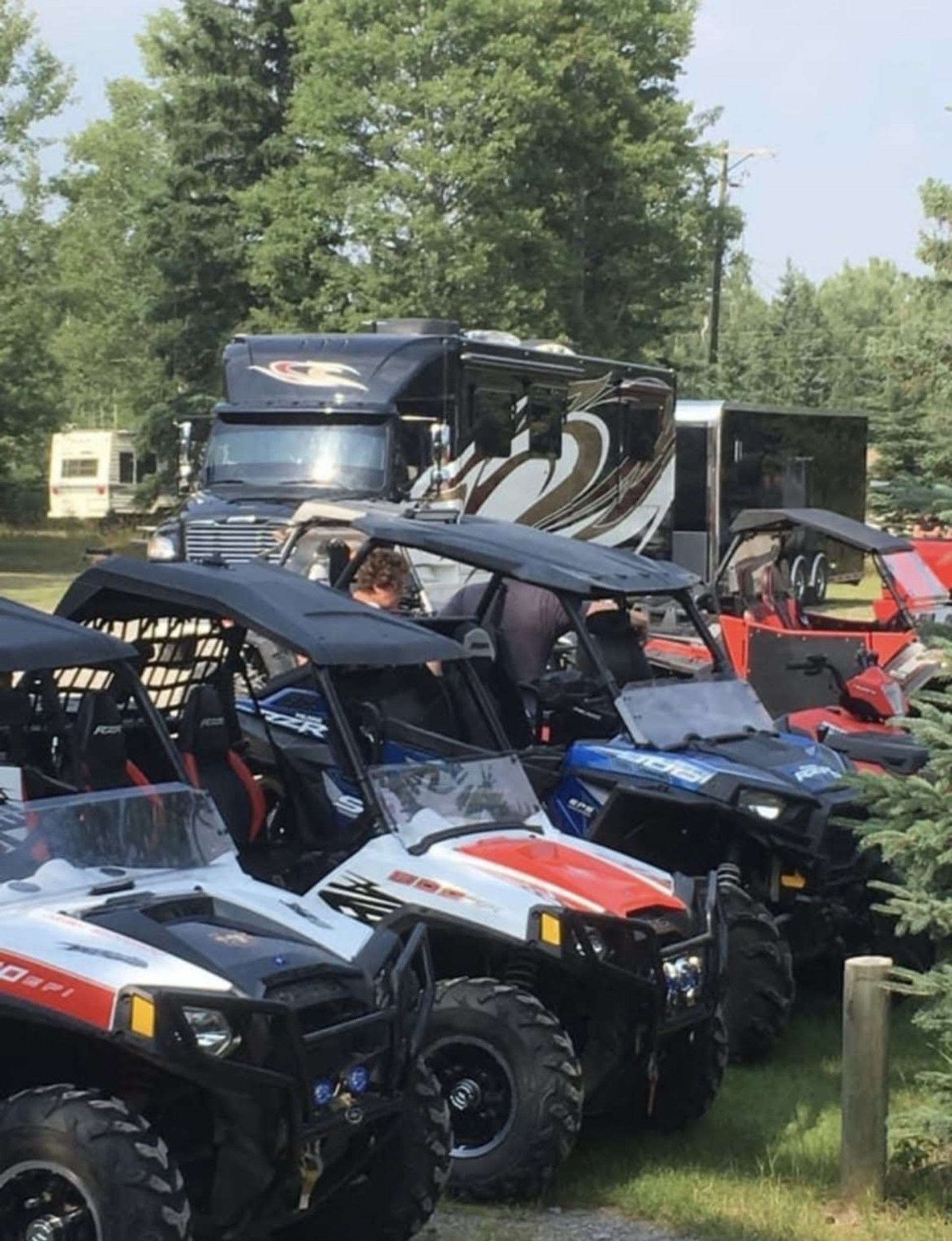 Off-road vehicles parked on grass in front of a motorhome and trailer.